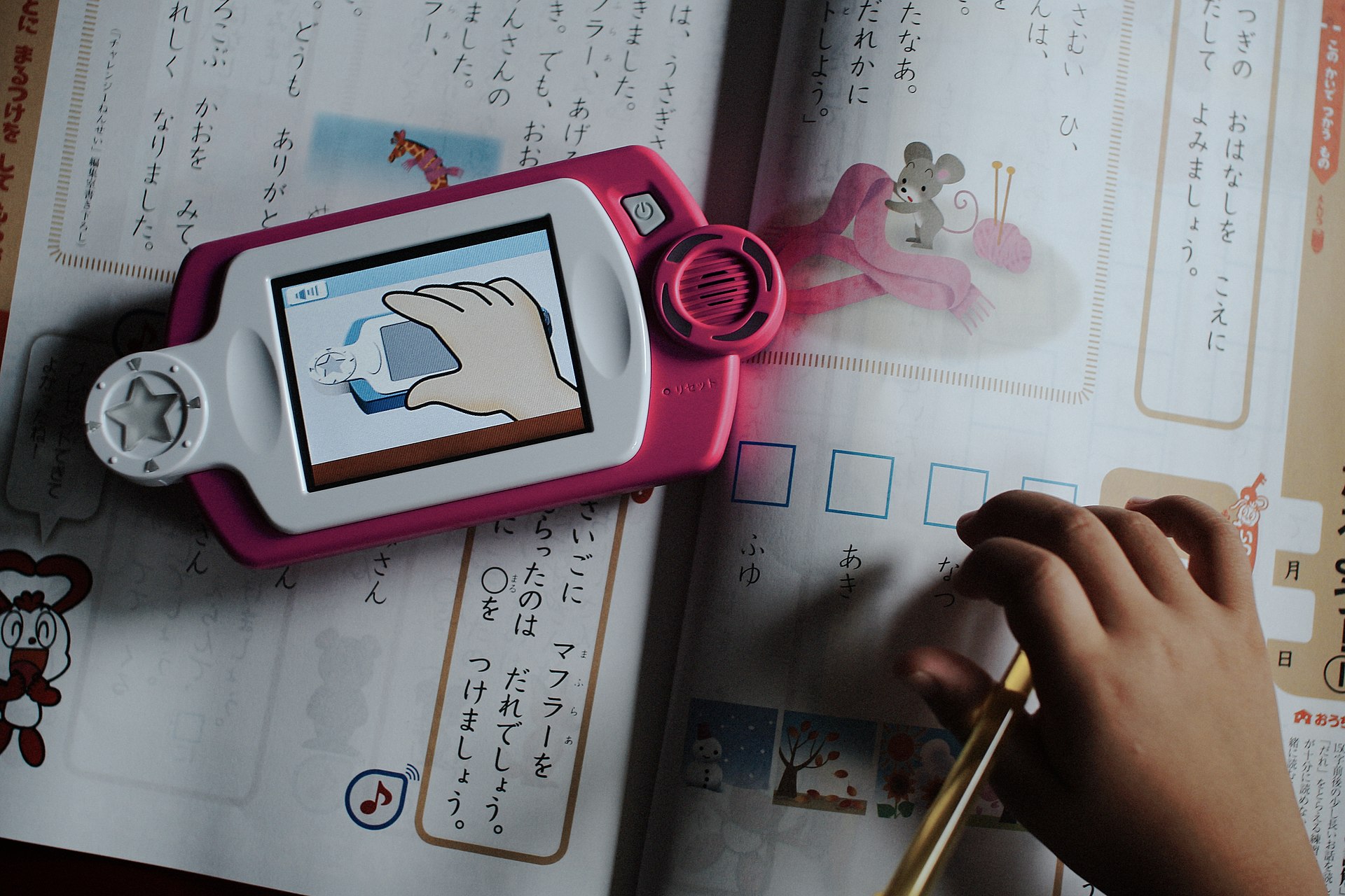 Digital Japanese learning device and stylus resting on an open workbook page
