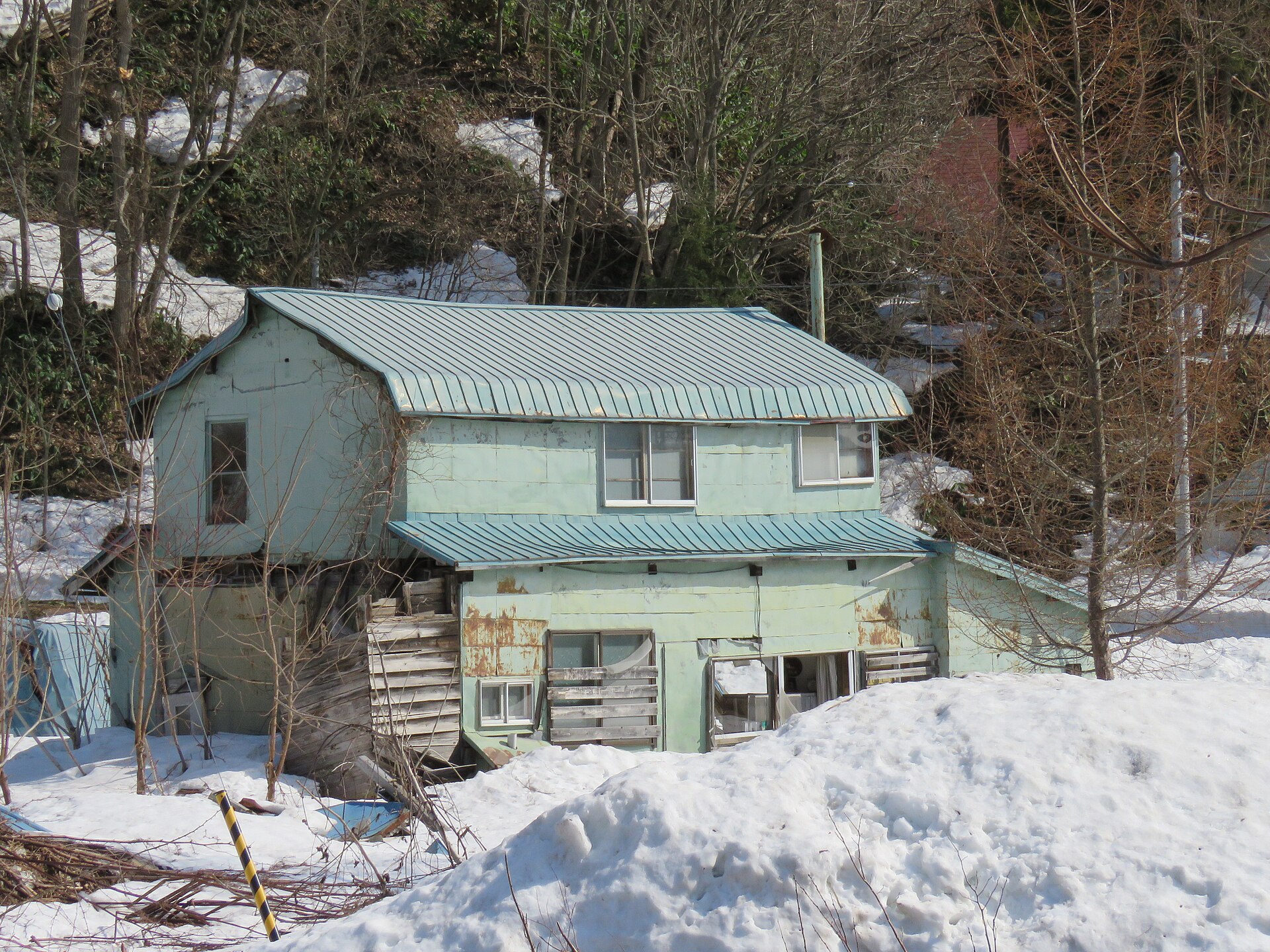 Verlassenes, verfallenes Wohnhaus mit rostigem Blechdach im Schnee in Mikasa, Hokkaido