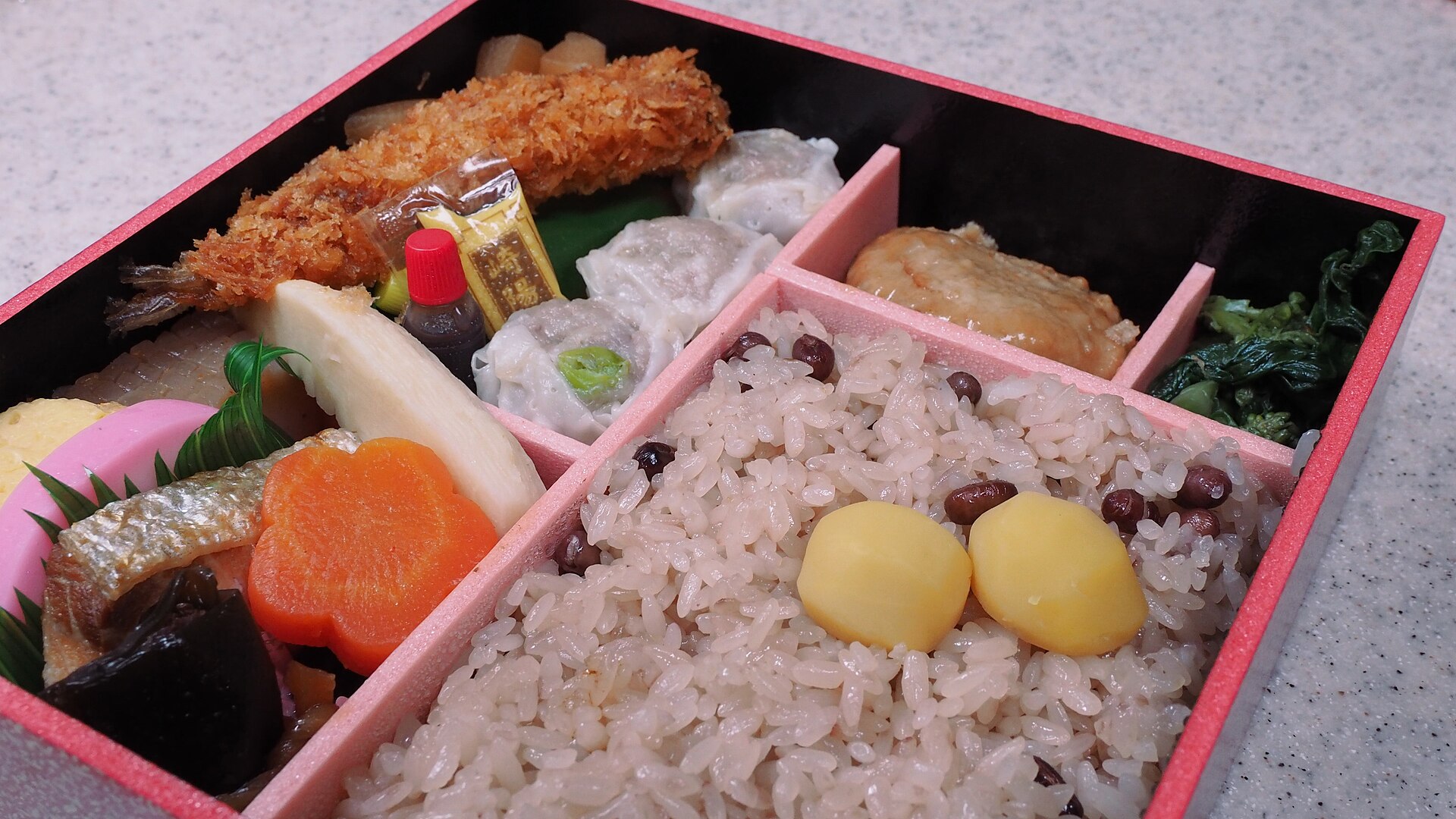 Nahaufnahme einer Bento-Box mit Reis, Frittiertem, Fischkuchen und Beilagen