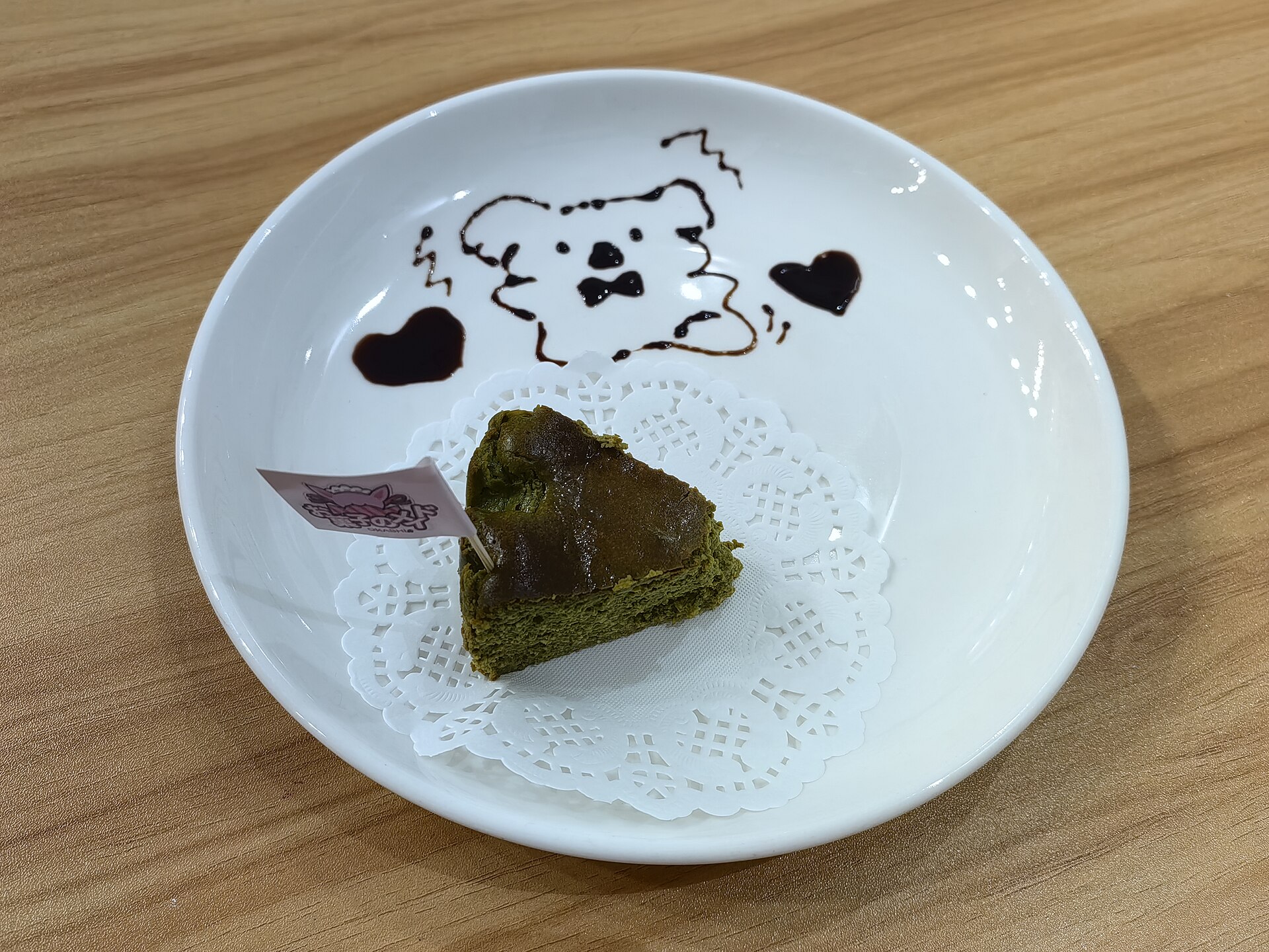 Ein Stück Matcha-Käsekuchen mit Schokoladensauce-Dekor auf weißem Teller