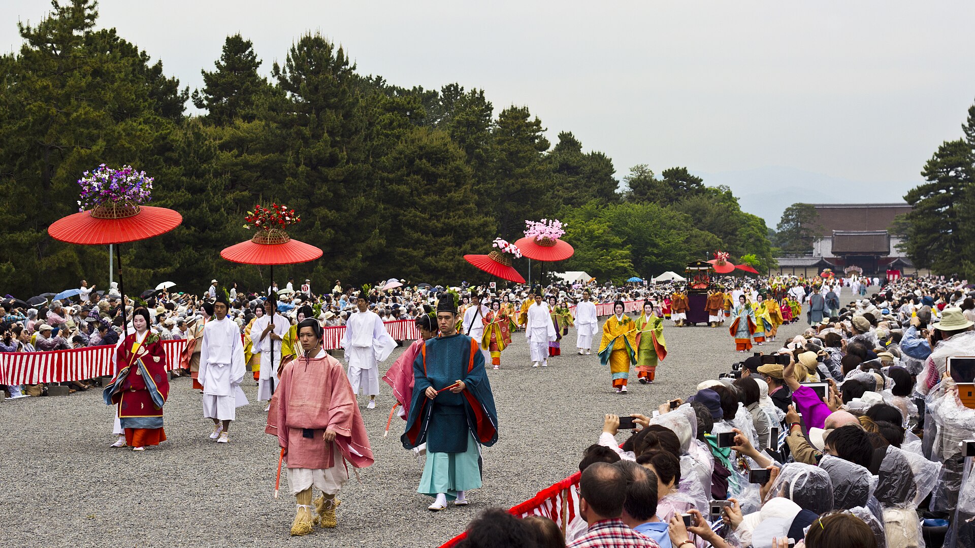 Heian-era procession of the Aoi Matsuri festival before the Kyoto Imperial Palace, with red ceremonial umbrellas