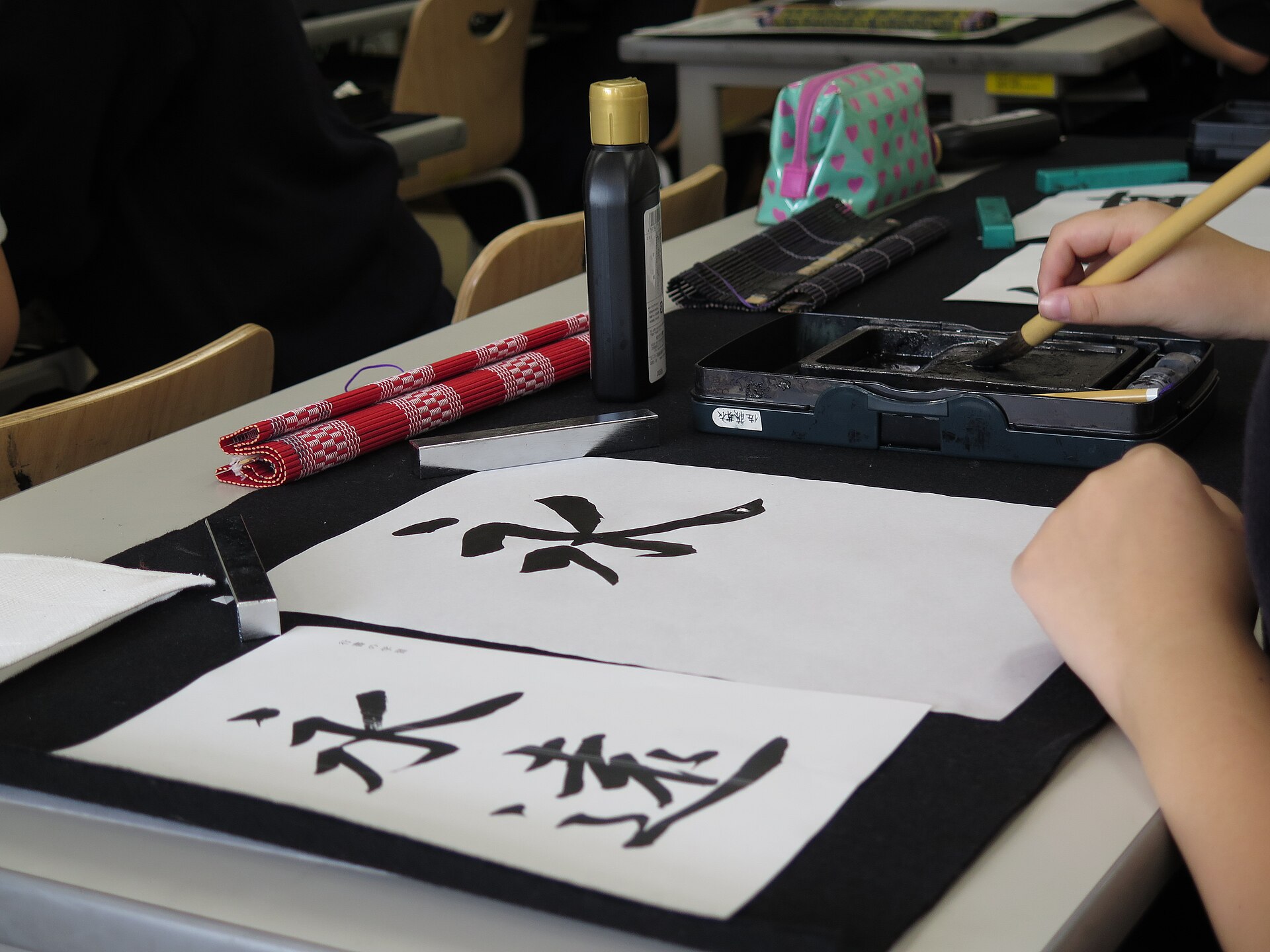 Hand practicing Japanese kanji calligraphy with brush and ink on washi paper