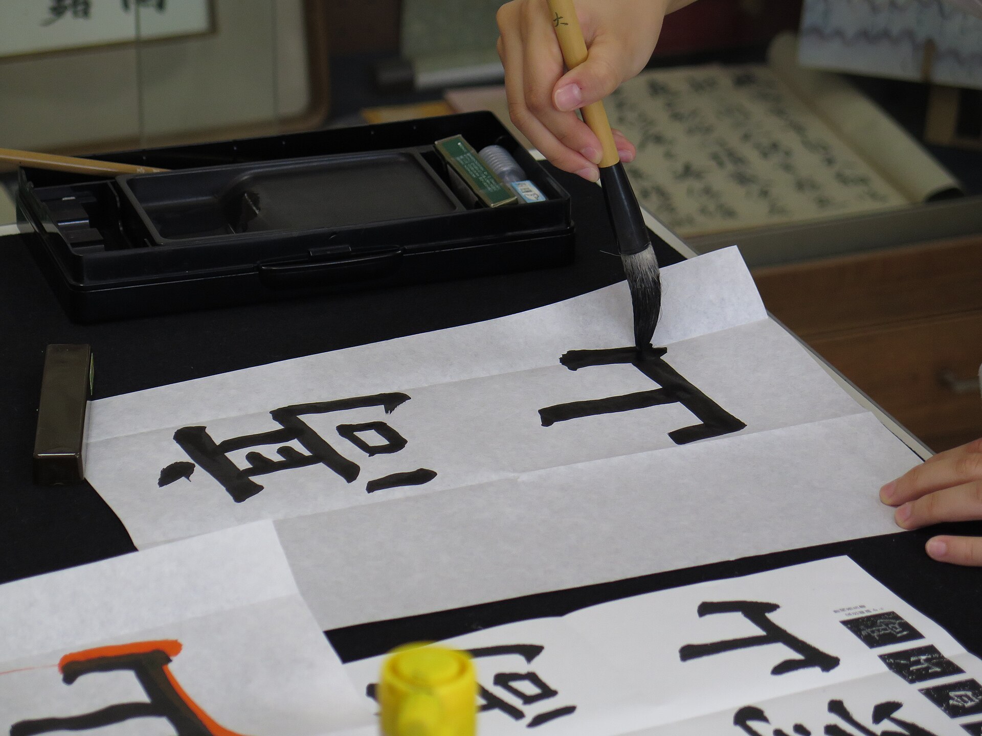 Close-up of a brush tip forming elaborate Japanese kanji calligraphy on paper
