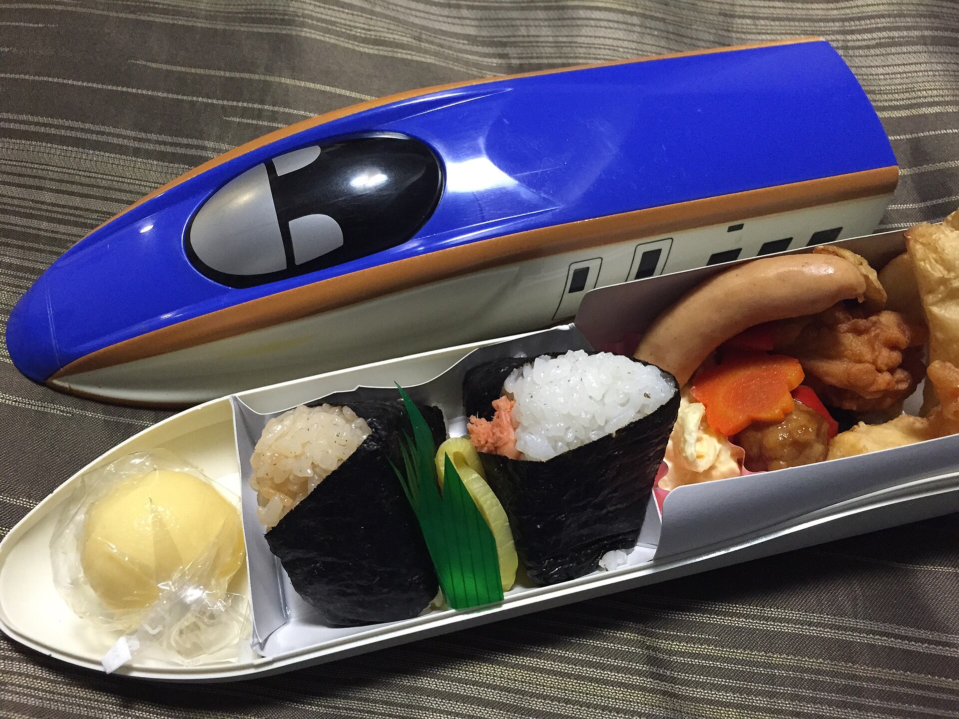 Ekiben station bento with onigiri, sausage and sides beside a shinkansen model